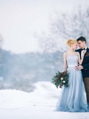 Bride and groom among snowy landscape. Bride and groom are standing and hugging. Winter wedding outdoors. Copy space.
