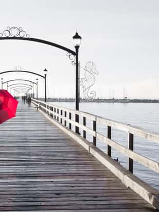 Woman holding a red umbrella walking on a rainy day on the pier in White Rock, British Columbia, Canada.
