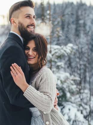 Bearded man and his lovely bride pose on the snow in a magic winter forest