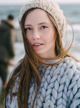 attractive young woman in merino wool sweater and hat on winter seashore