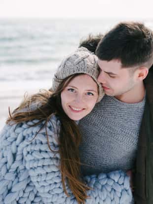 smiling couple hugging on winter sea shore and looking at camera