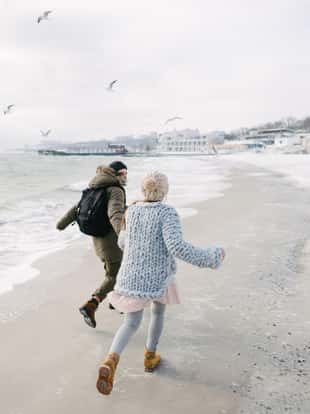 back view of young couple holding hands and running on winter seashore