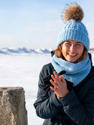Portrait beauty woman model on winter background. Beautiful modern urban young woman wearing blue knitting hat  basks in cold weather on the background of the frozen sea