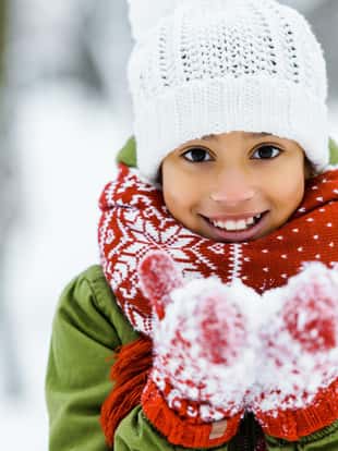 cute african american child showing white snow an smiling at camera in winter forest
