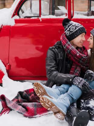 Cheerful couple in warm cozy clothes near red vintage car covered with snow in the garden. Cold happy winter day. Holidays, Christmas, New Year, winter, love, beauty concept.
