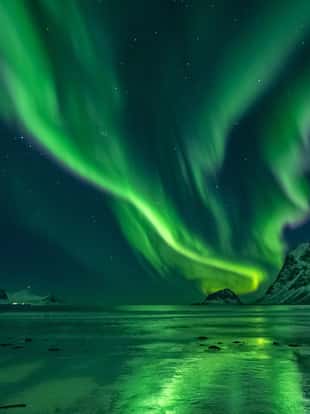 amazing clear night sky with aurora borealis over a beach with reflections, lofoten, norway