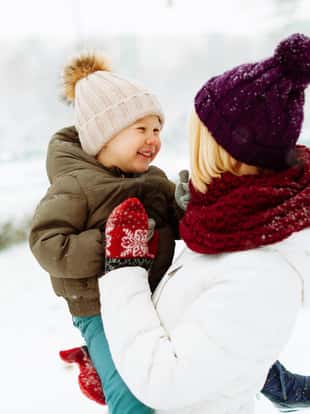 Photo of a handsome mother hugging her little boy, having time together in a winter walk