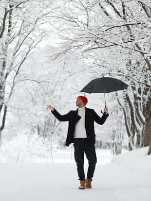 A man on a walk in the park. Young man with an umbrella under the winter snowfall.