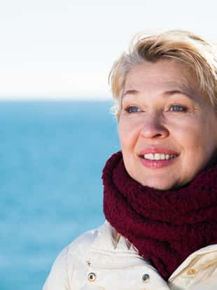 Senior woman taking walk by sea on sunny chilly day
