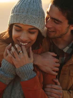 Close up portrait of affectionate young couple on winter holiday. Handsome young man embracing his girlfriend from behind in a winter day.