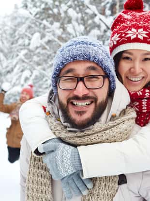 Amorous Asian couple on background of their friends playing snowballs on winter day