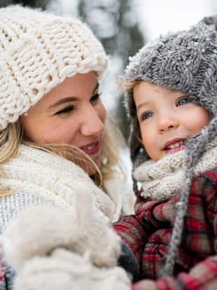 Side view of cheerful mother with small daughter standing in winter nature, laughing.