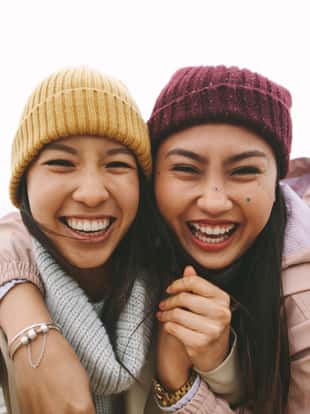 Happy asian woman in winter wear standing near the sea on a cold morning. Smiling women standing outdoors holding each other and having fun on a winter morning.