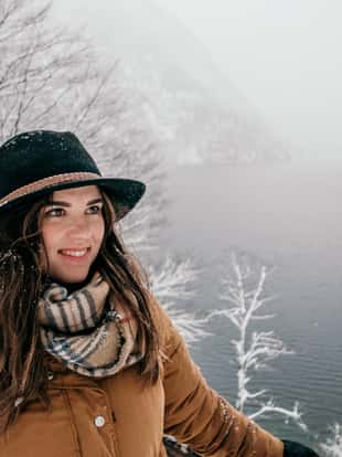 A beautiful Caucasian woman smiling in front of the water in the frozen forest with a hat