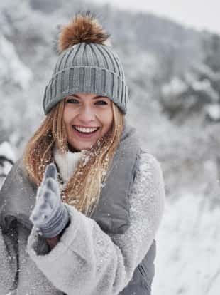 Conception of winter holidays. Cheerful girl in warm clothes playing with snow outdoors near the beautiful forest.