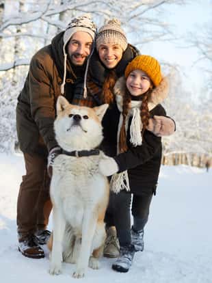 Full length portrait of happy family posing with dog in beautiful winter forest, copy space
