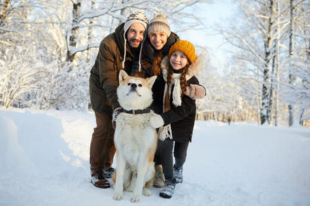 Full length portrait of happy family posing with dog in beautiful winter forest, copy space