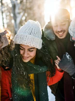 A group of young cheerful friends on a walk outdoors in snow in winter forest, having fun.