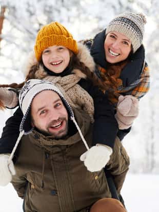 Portrait of playful happy family in winter forest looking at camera and smiling, copy space