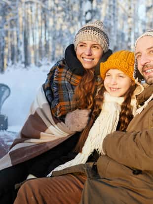 Portrait of happy family sitting on bench in beautiful winter forest posing together and looking away, copy space