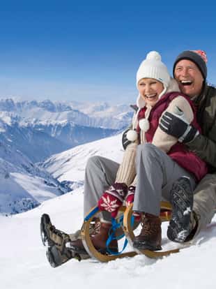 Laughing senior couple on winter vacation riding sled down mountain