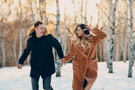 Loving young couple walking playing and having fun in winter forest park.
