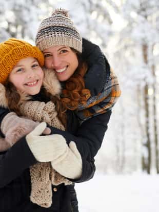 Waist up portrait of loving mother embracing cute little girl in winter forest and smiling at camera, copy space