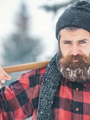 New year man in snowy cold forest. Man with beard in winter forest with snow hold axe. Wanderlust, hiking and travel. Christmas hipster lumberjack with ax in wood.. Winter holiday and celebration.
