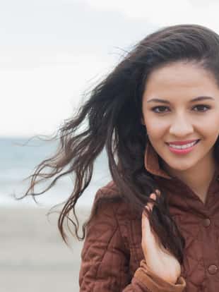 Portrait of a cute smiling young woman in stylish brown jacket on the beach