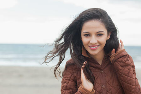 Portrait of a cute smiling young woman in stylish brown jacket on the beach