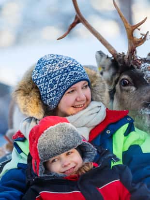 Family of mother and little girl at reindeer safari in winter forest in Lapland Finland