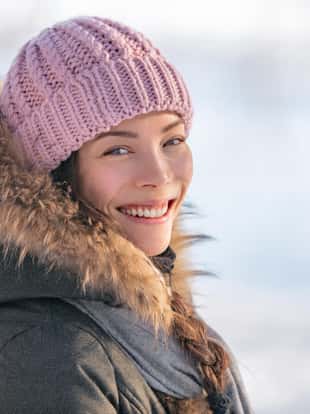 Winter woman portrait in cold outdoor nature. Asian girl model wearing wool hat and fur jacket outside in winter background, natural beauty.