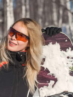 Young adult woman snowboarder holding board in heand in snow winter