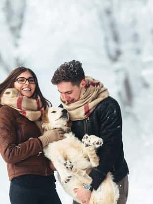 Cute young hipster couple having fun in winter park with their dog on a bright day and smiling
