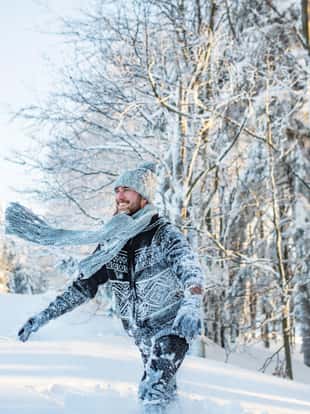 Young man having fun outdoors in winter, jumping in snow.