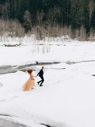 Young newlywed couple walking in the winter forest in the snow. The bride and groom are hugging in the park iBeautiful men and women in wedding dresses