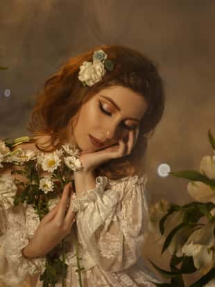 A tender girl in a white vintage dress with open shoulders hugs the flowers. Background of the clouds and light haze.