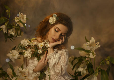 A tender girl in a white vintage dress with open shoulders hugs the flowers. Background of the clouds and light haze.