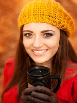 Beautiful young woman drinking hot drink in park