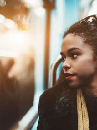 The portrait of a young charming African-American female pensively looking outside the carriage window while sitting indoors of a metro train; Brazilian girl in a subway train, shallow depth of field