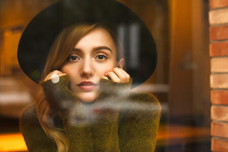 Beautiful young blonde woman sitting in the coffee bar in long autumn evening. She is wearing nice warm clothes and looking outside through the window. Very nice atmosphere and feelings made by colors.