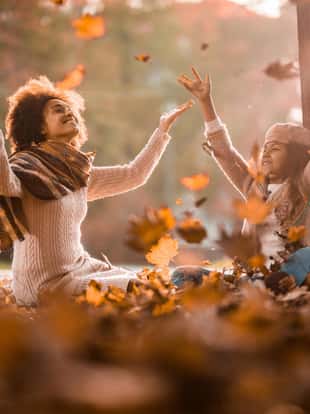 Carefree black mother and daughter having fun while throwing autumn leaves in nature.