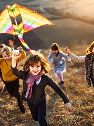 Large group of carefree kids running with a kite up the hill in autumn day. Focus is on boy with a kite looking at camera.