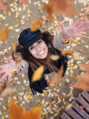 Shot of pretty young woman looking to the sky with arms raised as leaves fall from the trees in the park in autumn.