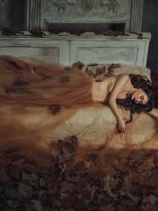 Tale of Sleeping Beauty. The girl is in the old, abandoned room. It covered the dust and leaves. Autumn atmosphere of sadness. Beautiful, long, wavy hair.  Princess lying on the bed.  Creative colors