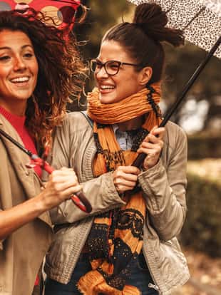 Two female best friend walks at the city street with umbrellas above head.They smiling and making fun.Raining day and autumn concept.
