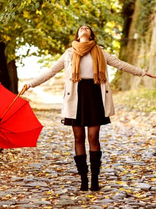 Young brunette woman walking with a red umbrella on the stone path.