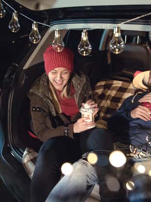 Young couple in love sitting in car open trunk