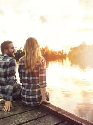 Cheerful young couple sitting on a lake pier chating. Lake Kaniere, New Zealand.
