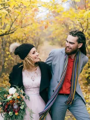 A happy couple is walking on a trail in an autumn forest. Bride and groom with dreadlocks are looking at each other on nature. Wedding ceremony outdoors.. Close-up portrait